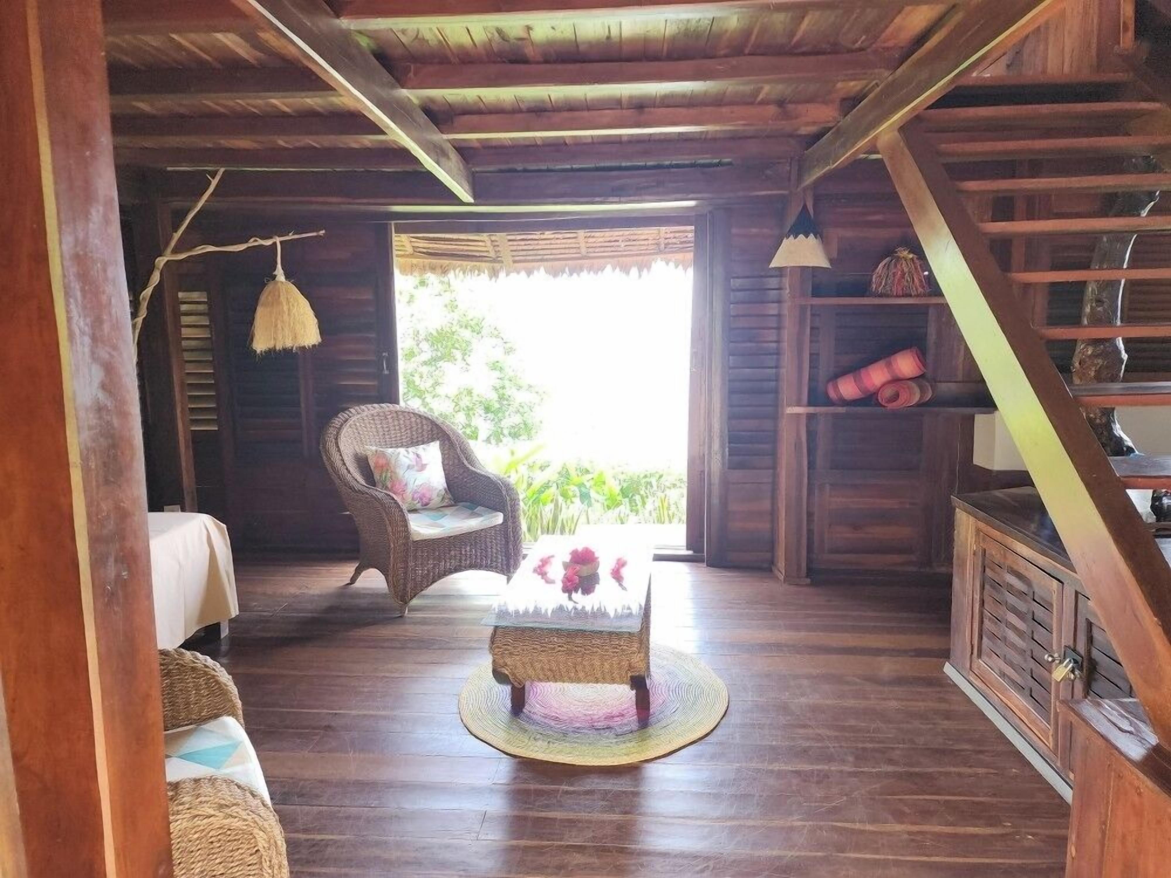 A wooden interior with a wicker chair, a small round table, and a staircase.