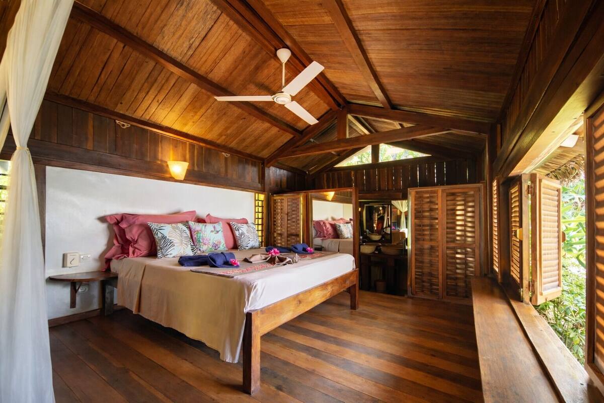 A wooden room with a bed, a ceiling fan, and a small table.