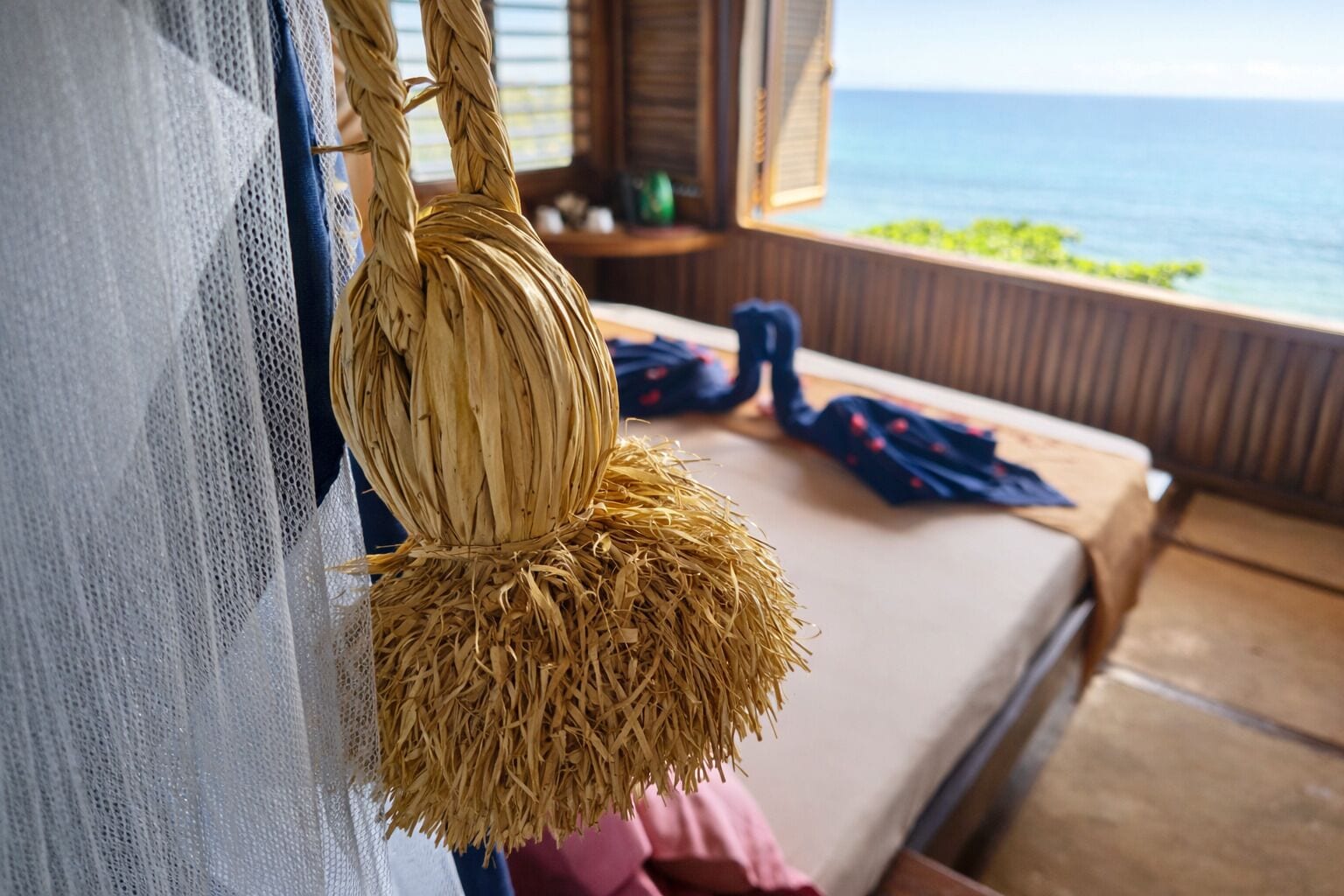 A room with a bed, a hanging basket, and a view of the ocean.