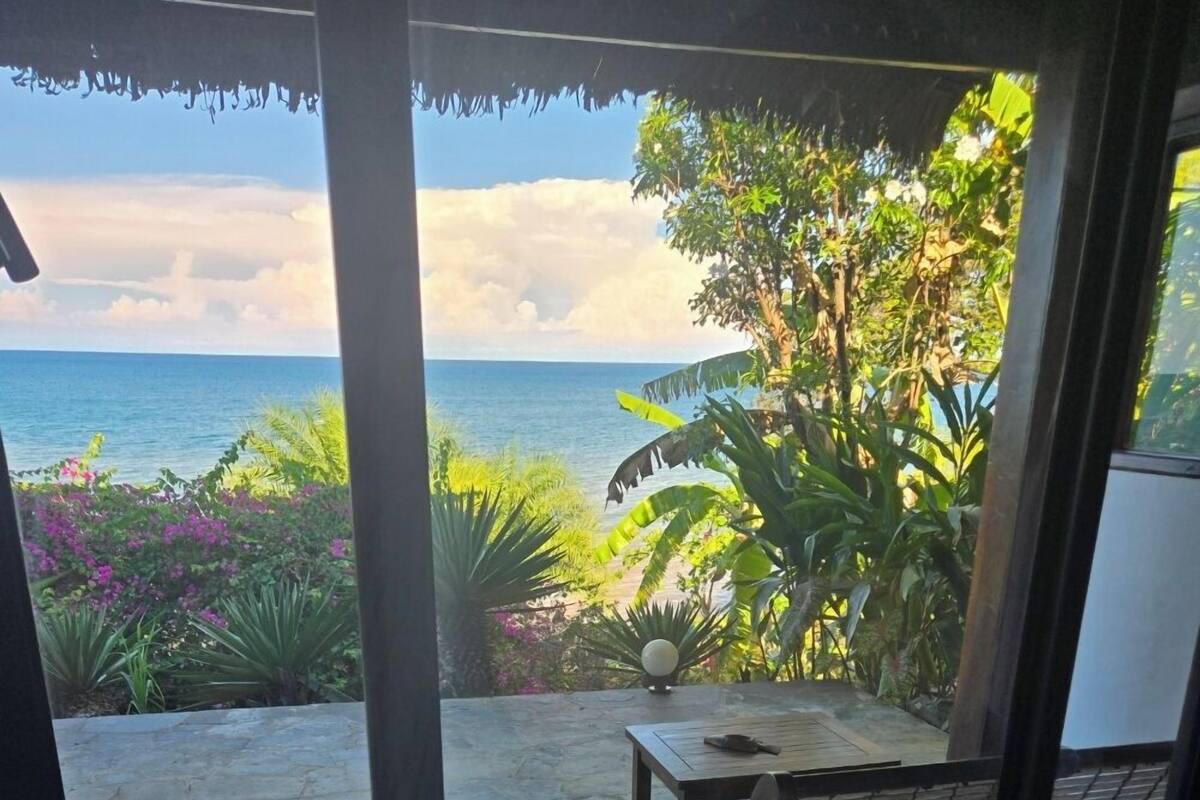 A room with a view of the sea, a stone patio, and a table with a chair.