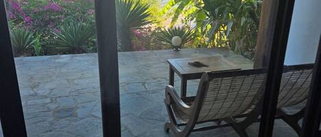 A room with a view of the sea, a stone patio, and a table with a chair.