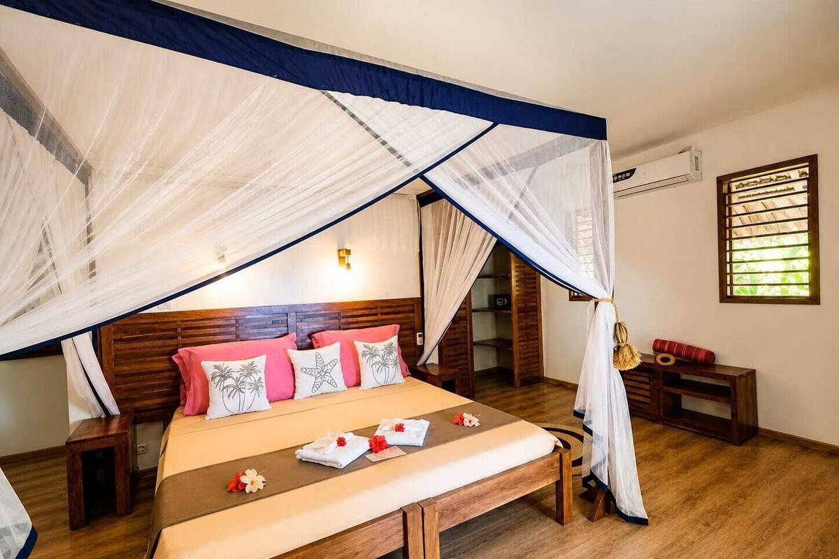 A bedroom with a bed, bedside tables, a bench, and a window with blinds.