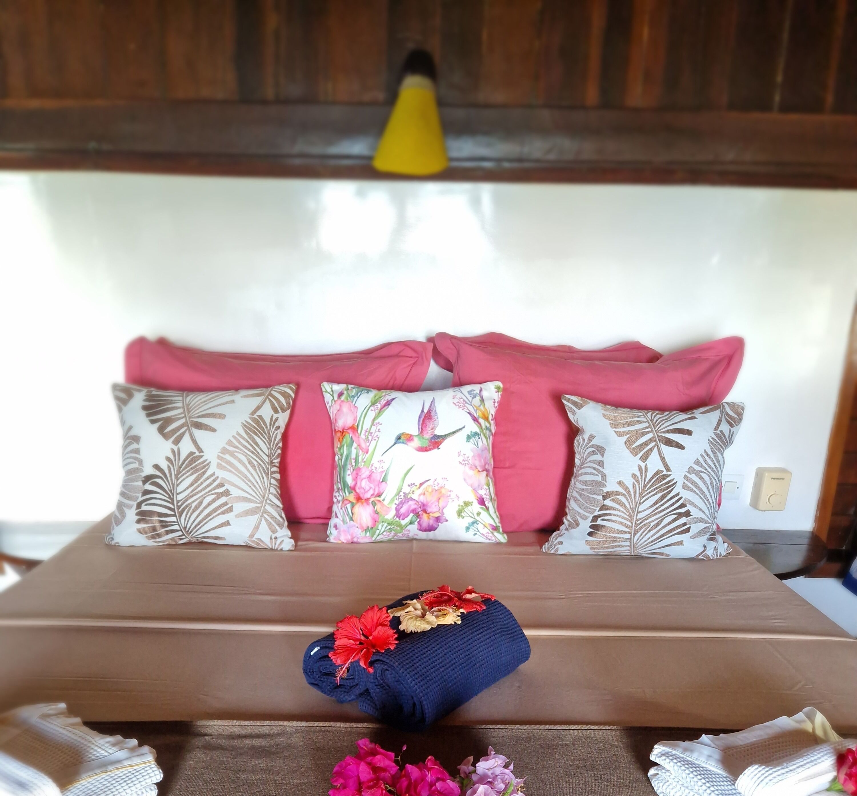 Un lit avec plusieurs oreillers, un coussin décoratif orné de motifs floraux et un petit coussin bleu avec des fleurs rouges.