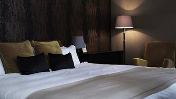 A hotel room with a bed, pillows, a nightstand, a lamp, and a chair.