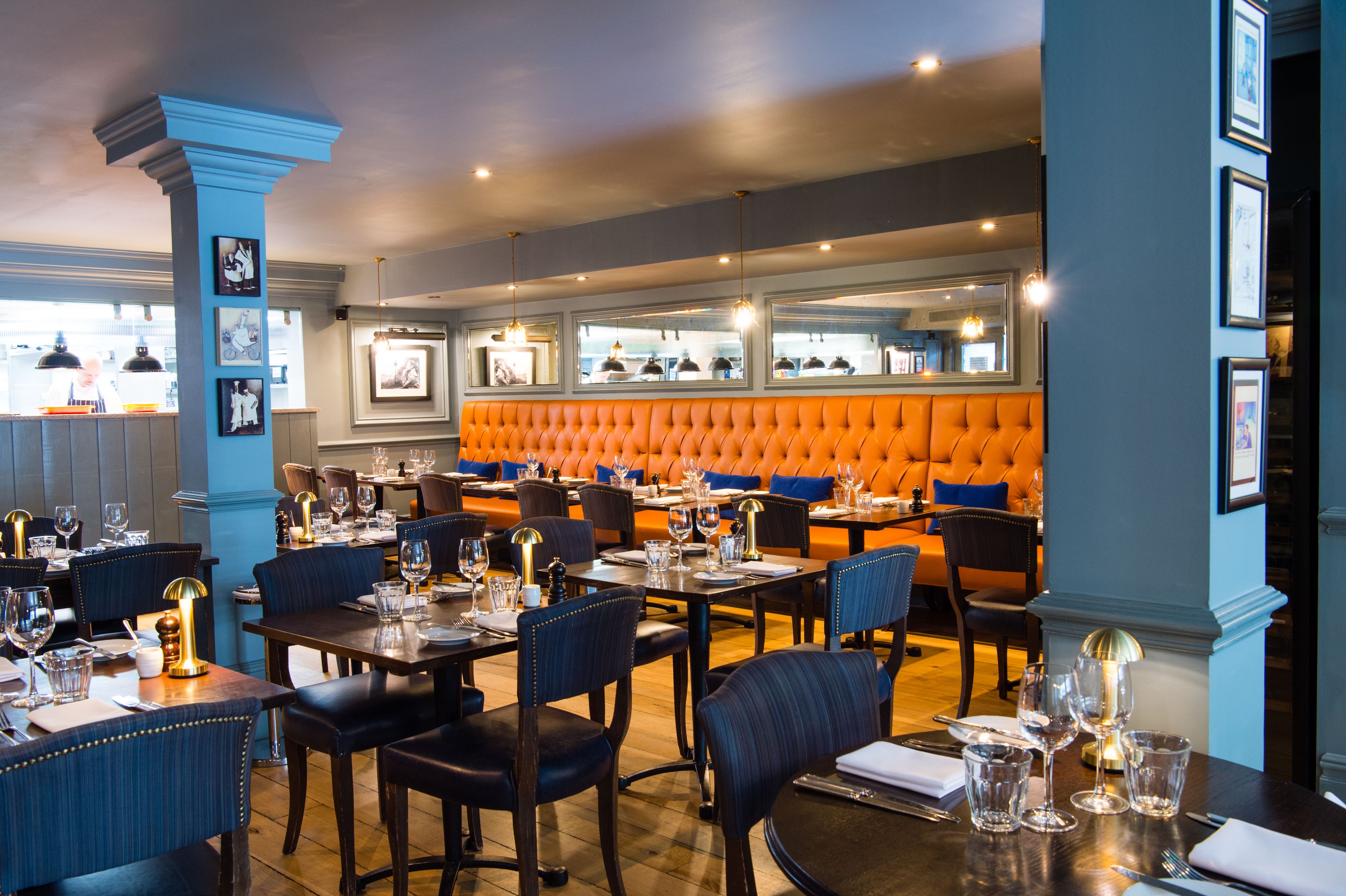 A restaurant with a modern interior, featuring a mix of blue and orange seating, wooden tables, and framed pictures on the walls.