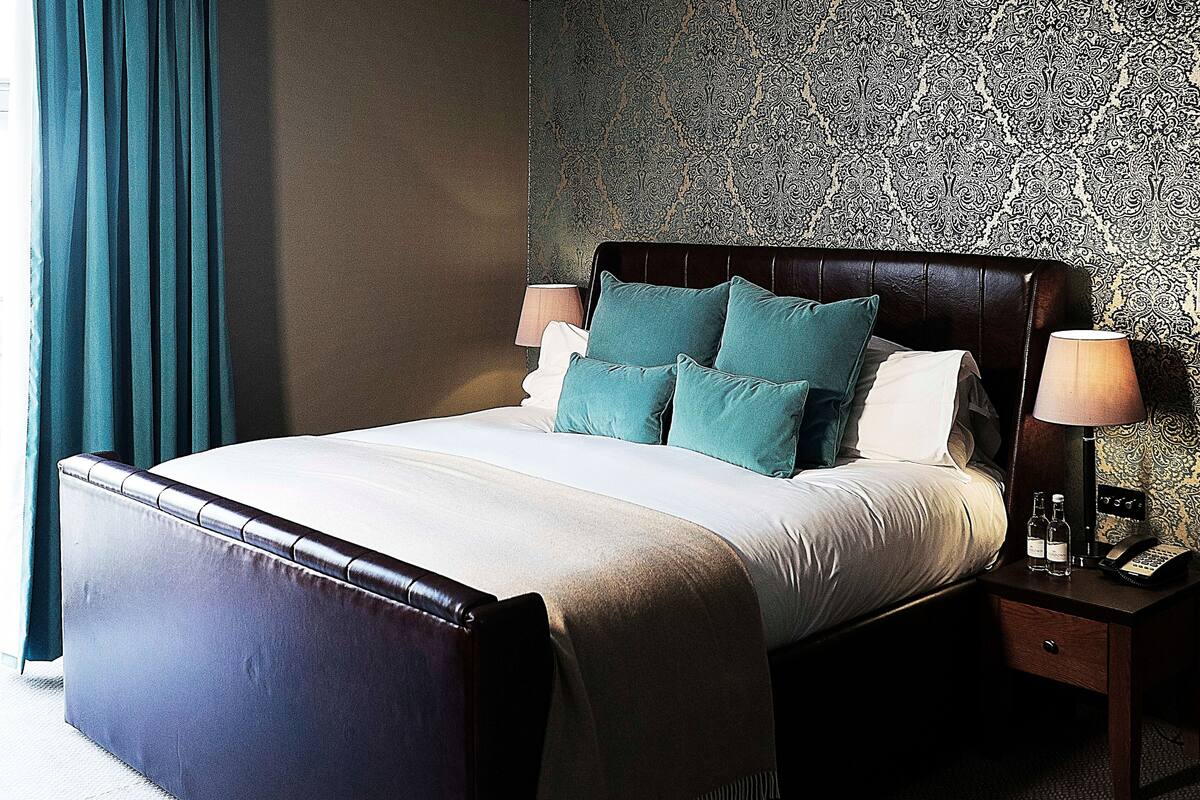A neatly made bed with a dark headboard, two bedside lamps, and a nightstand with a telephone and two bottles.