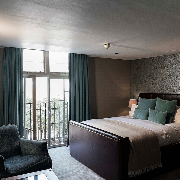A hotel room with a large bed, a chair, a window with curtains, and a patterned wall. - Hotel du Vin & Bistro Cambridge (Cambridge)