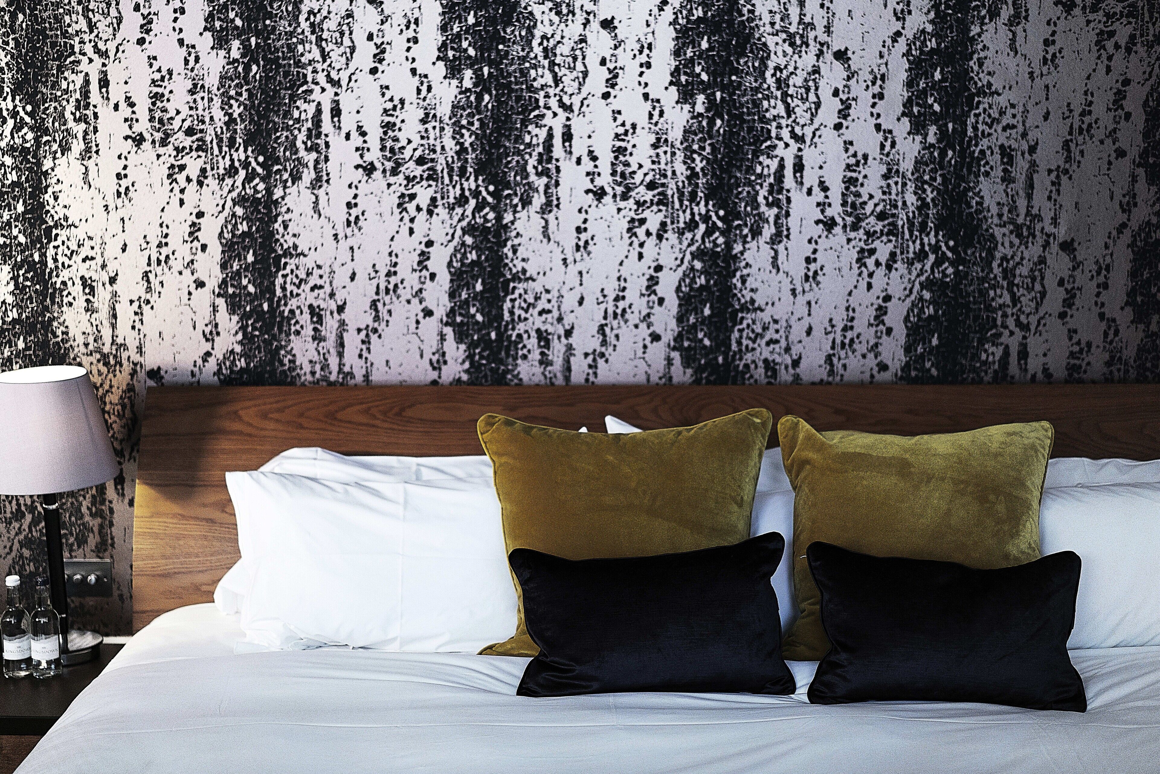 A neatly made bed with white sheets and two pillows, one in a mustard color and the other in black, against a textured wall.