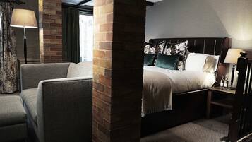 A hotel room with a brick column, a bed with a headboard, a nightstand, a lamp, and a view of the outside.
