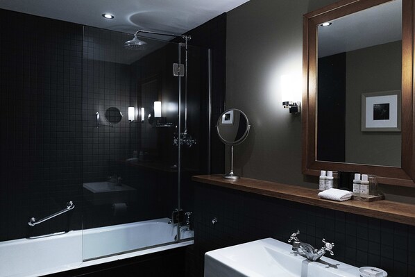 A modern bathroom with a glass-enclosed shower, a white bathtub, and a vanity with a mirror and toiletries.