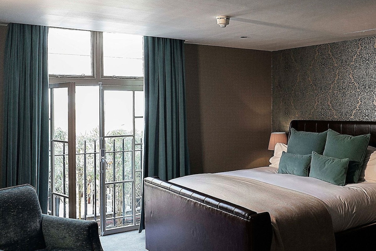 Een hotelkamer met een bed, een stoel, een raam met gordijnen en een behang met patroon.