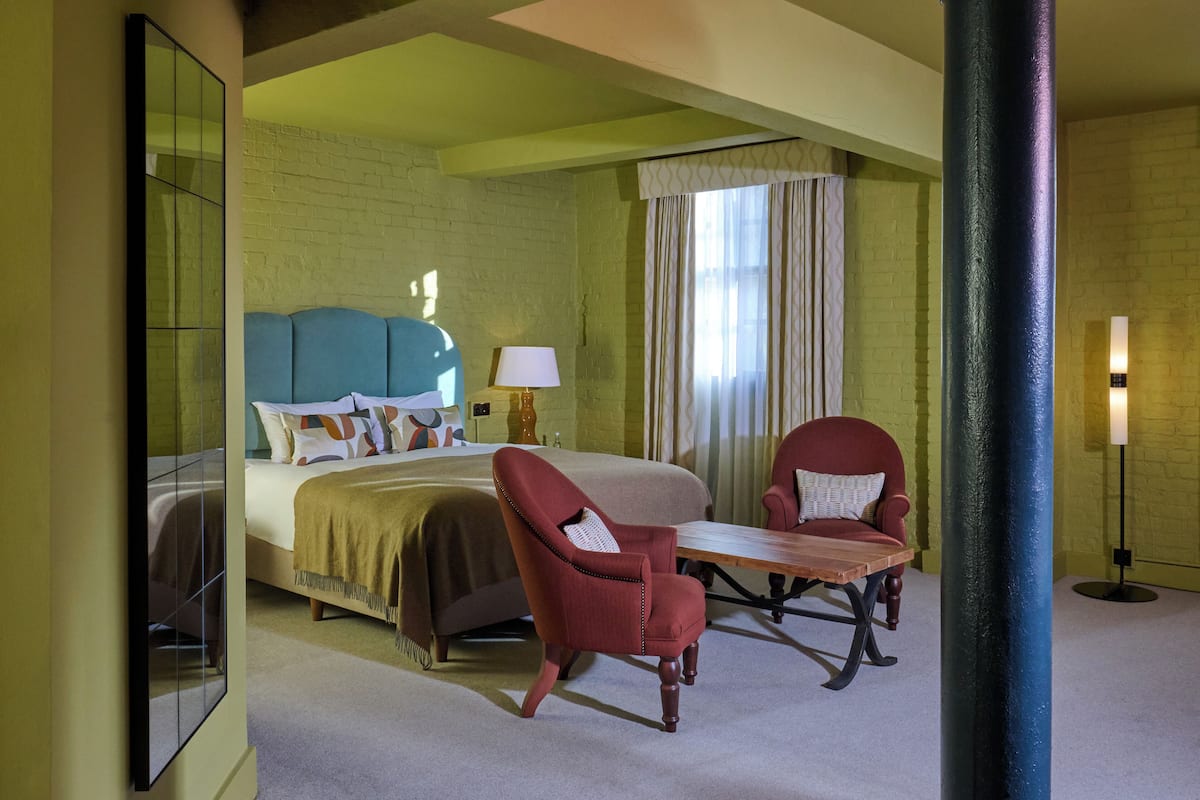 Ein Hotelzimmer mit einem Bett, zwei Sesseln, einem Tisch, einer Lampe und einem großen Spiegel.