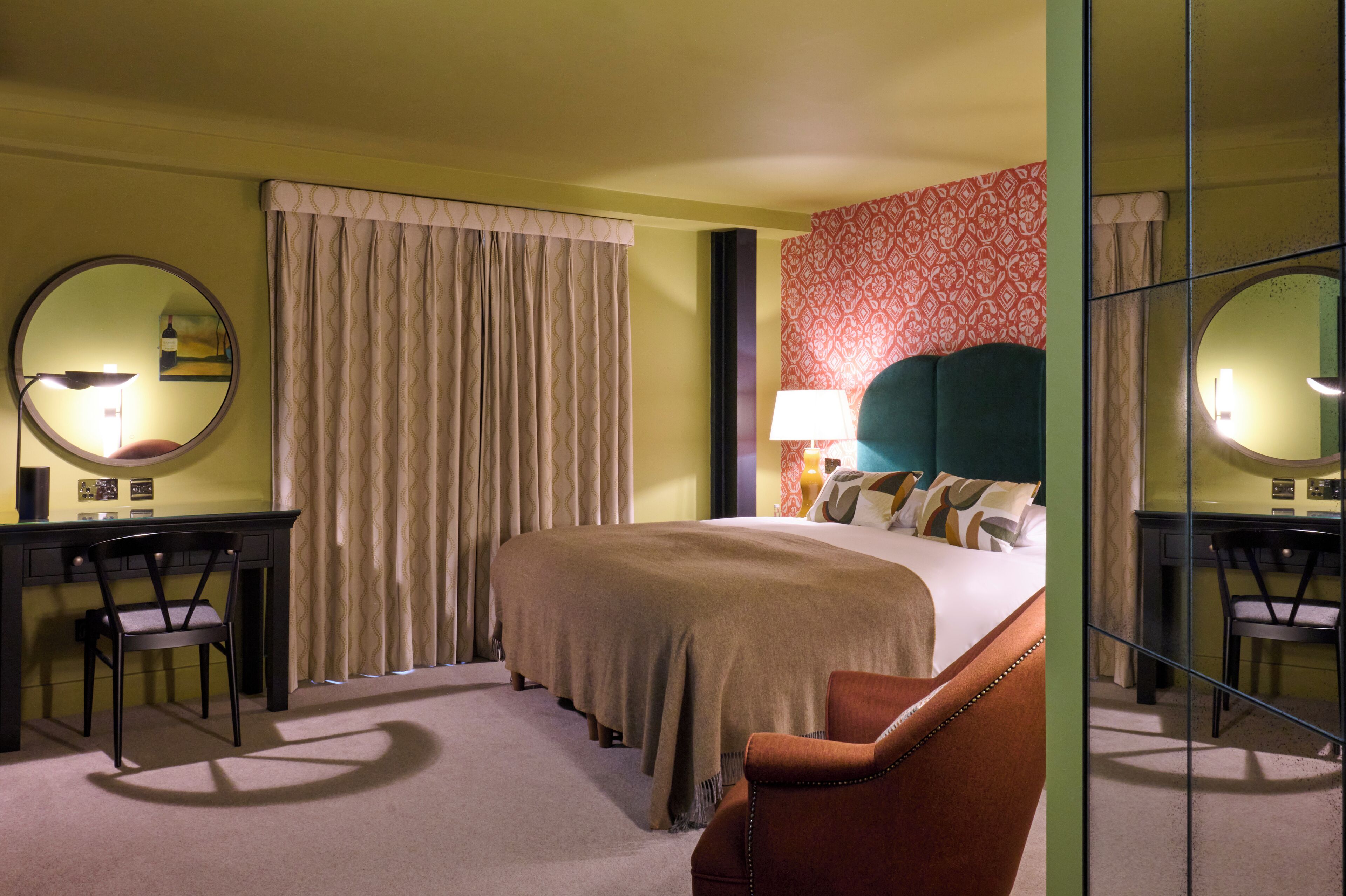 Une chambre d’hôtel avec un lit, un bureau, une chaise, un miroir et un mur décoré de motifs.