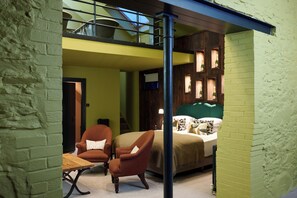 Una stanza con un letto, due poltrone, un tavolo e vista su un balcone.