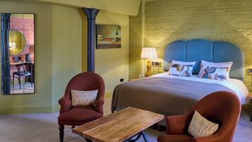 A hotel room with a large bed, two armchairs, a wooden table, a mirror, and a brick wall.