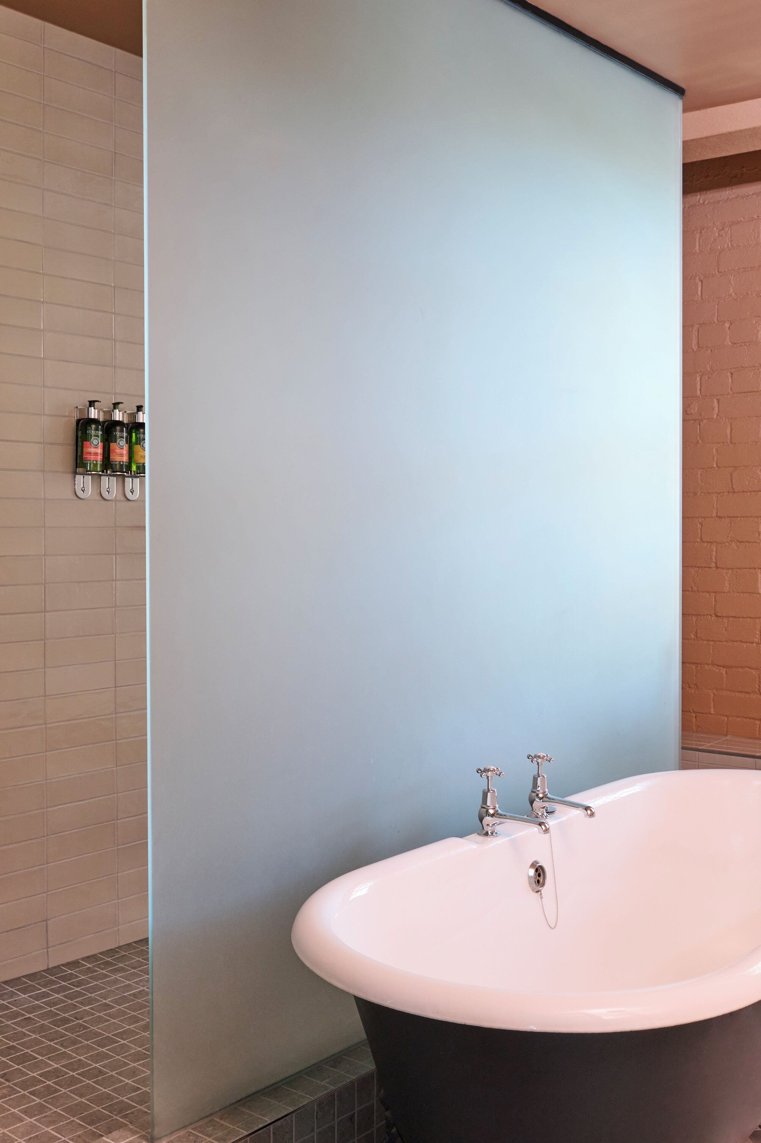 A modern bathroom with a freestanding bathtub, a tiled shower area, and a wall-mounted soap dispenser.