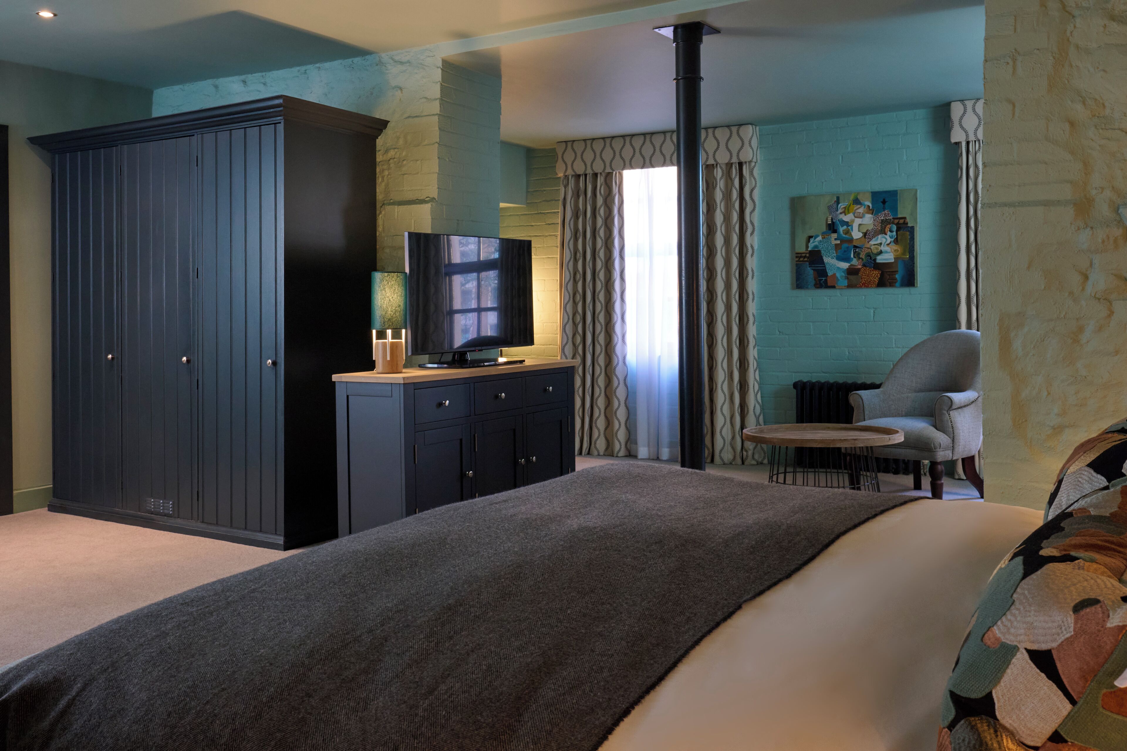 A bedroom with a large bed, a wardrobe, a television, a chair, and a painting on the wall.