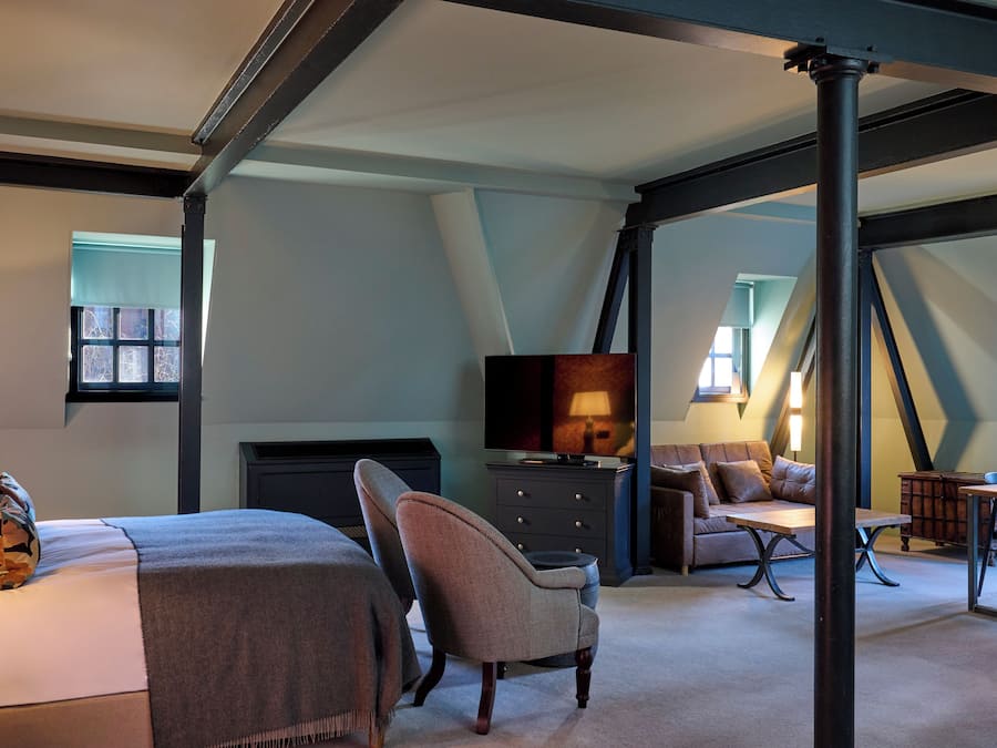A bedroom with a bed, a chair, a dresser, a television, and a desk with a lamp.