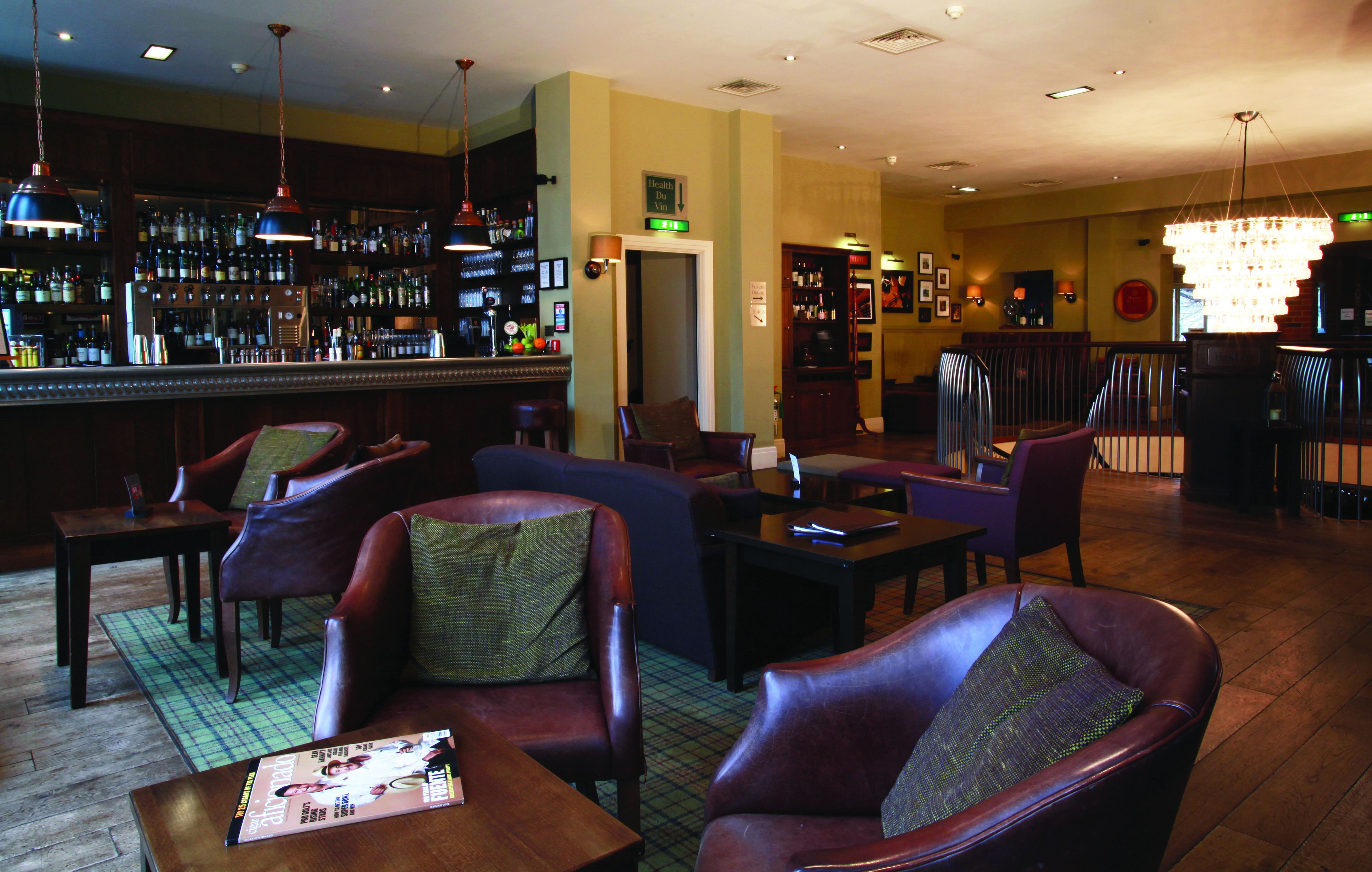 A bar area with leather chairs, a bar counter with bottles, and a chandelier.