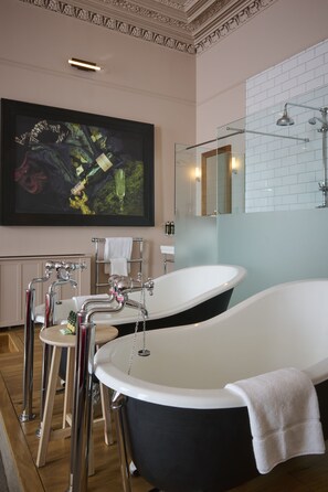 Een moderne badkamer met twee losstaande badkuipen, een groot kunstwerk in een lijst en een douchecabine met glazen wanden.