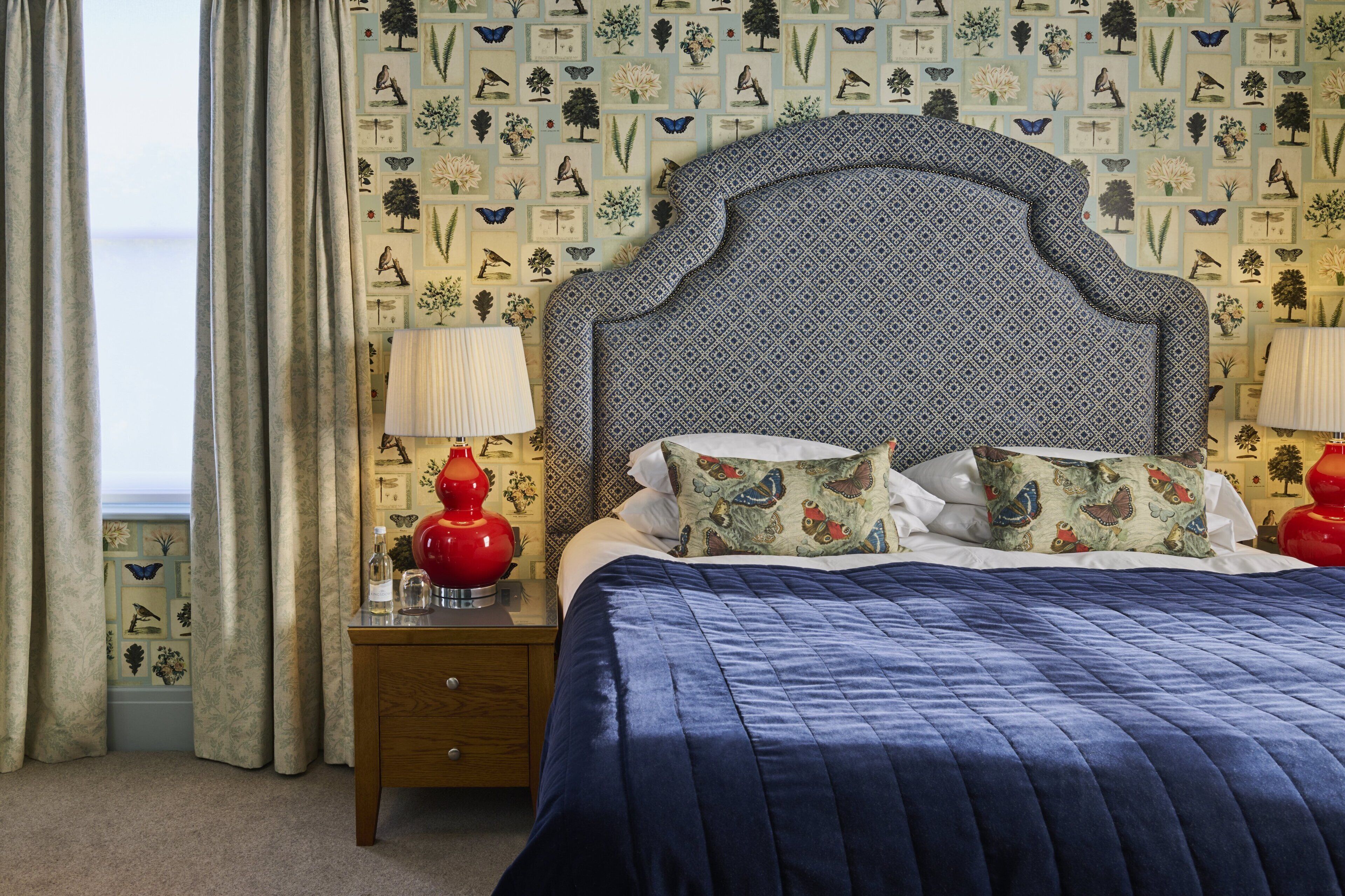 A bedroom with a patterned headboard, a blue quilted bedspread, and a nightstand with a lamp.