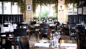 A restaurant with multiple tables and chairs, a wine rack with various bottles, and large windows with greenery outside. - Hotel du Vin & Bistro Cheltenham (Cheltenham)