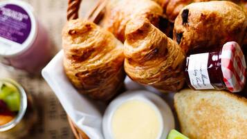 Una bandeja de desayuno con croissants, tostadas, mantequilla, mermelada y un vaso de jugo de naranja.