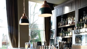 A bar area with wooden cabinets, hanging pendant lights, and a variety of bottles and glasses on shelves. - Hotel du Vin & Bistro Cheltenham (Cheltenham)