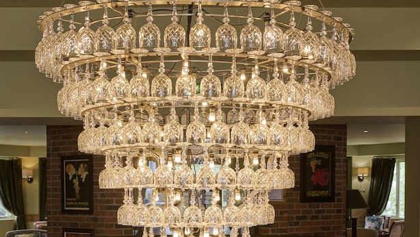 A grand chandelier with multiple tiers of crystal, a wooden staircase, and a dining area with tables and chairs. - Hotel du Vin & Bistro Cheltenham (Cheltenham)