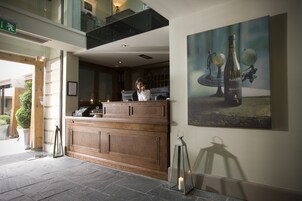 A reception area with a wooden counter, a framed artwork of a bottle and globe, and a stone floor.