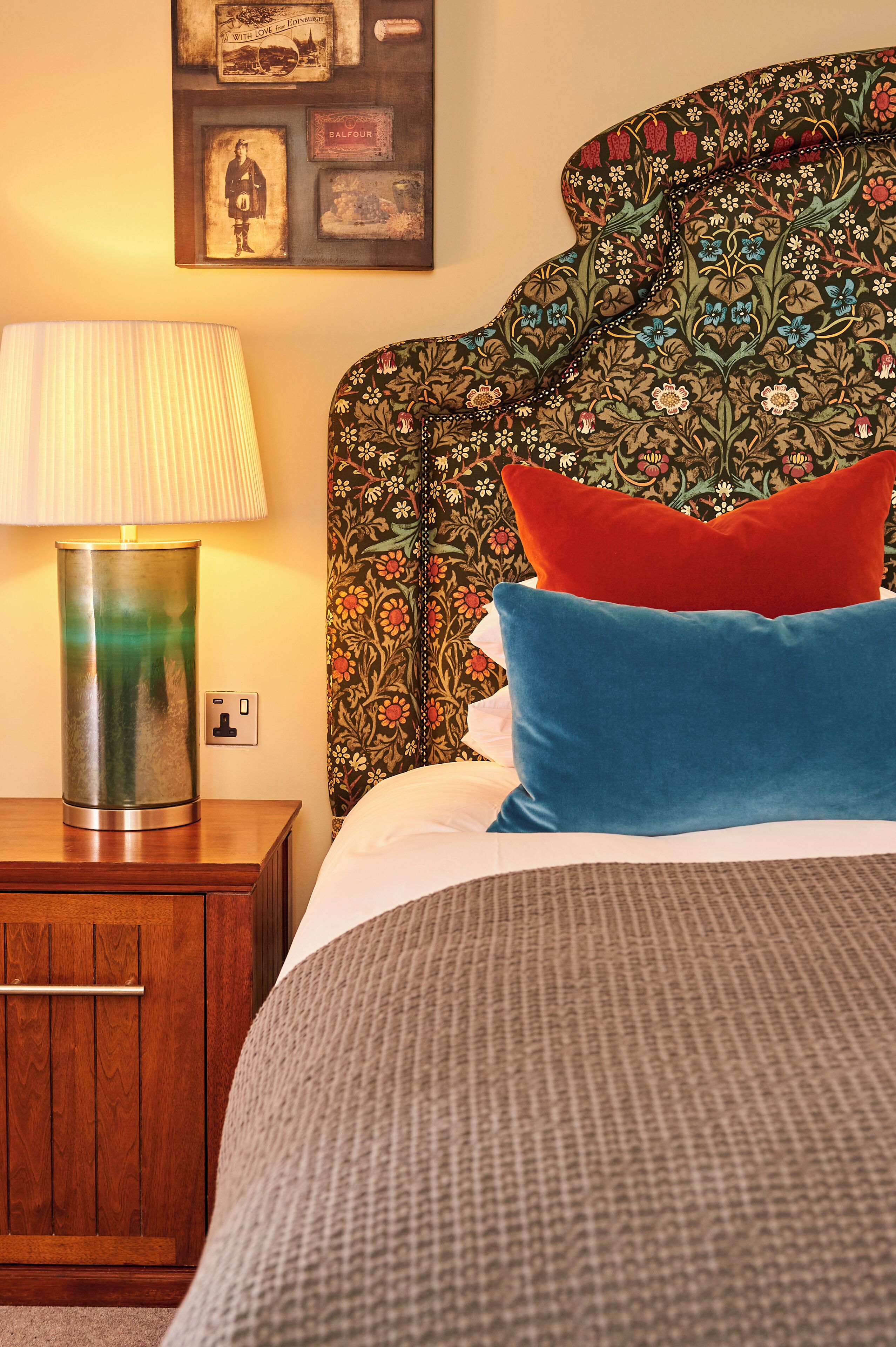 A neatly made bed with a patterned headboard, a bedside lamp, and a wooden nightstand.
