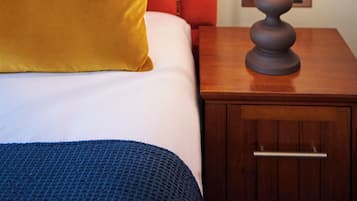 A neatly made bed with a red headboard, a mustard-colored pillow, and a blue patterned pillow. A wooden nightstand with a lamp is beside the bed.