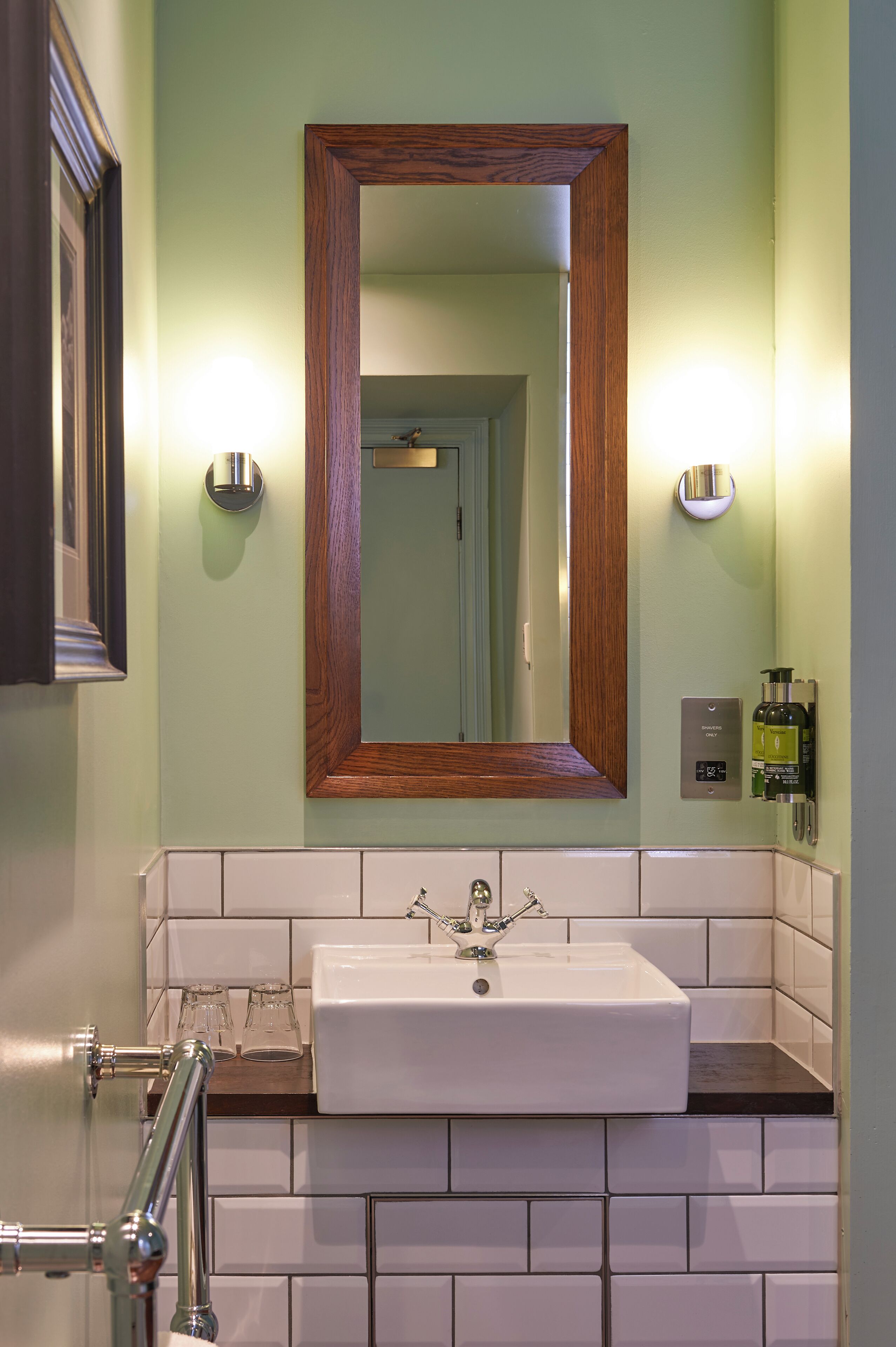 Une salle de bain avec un lavabo blanc, un miroir encadré en bois et deux appliques murales.
