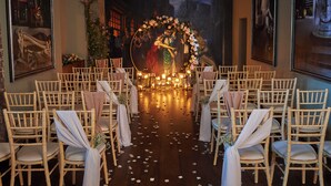 Preparació d'una cerimònia nupcial amb files de cadires, decoracions florals i un fons pictòric.