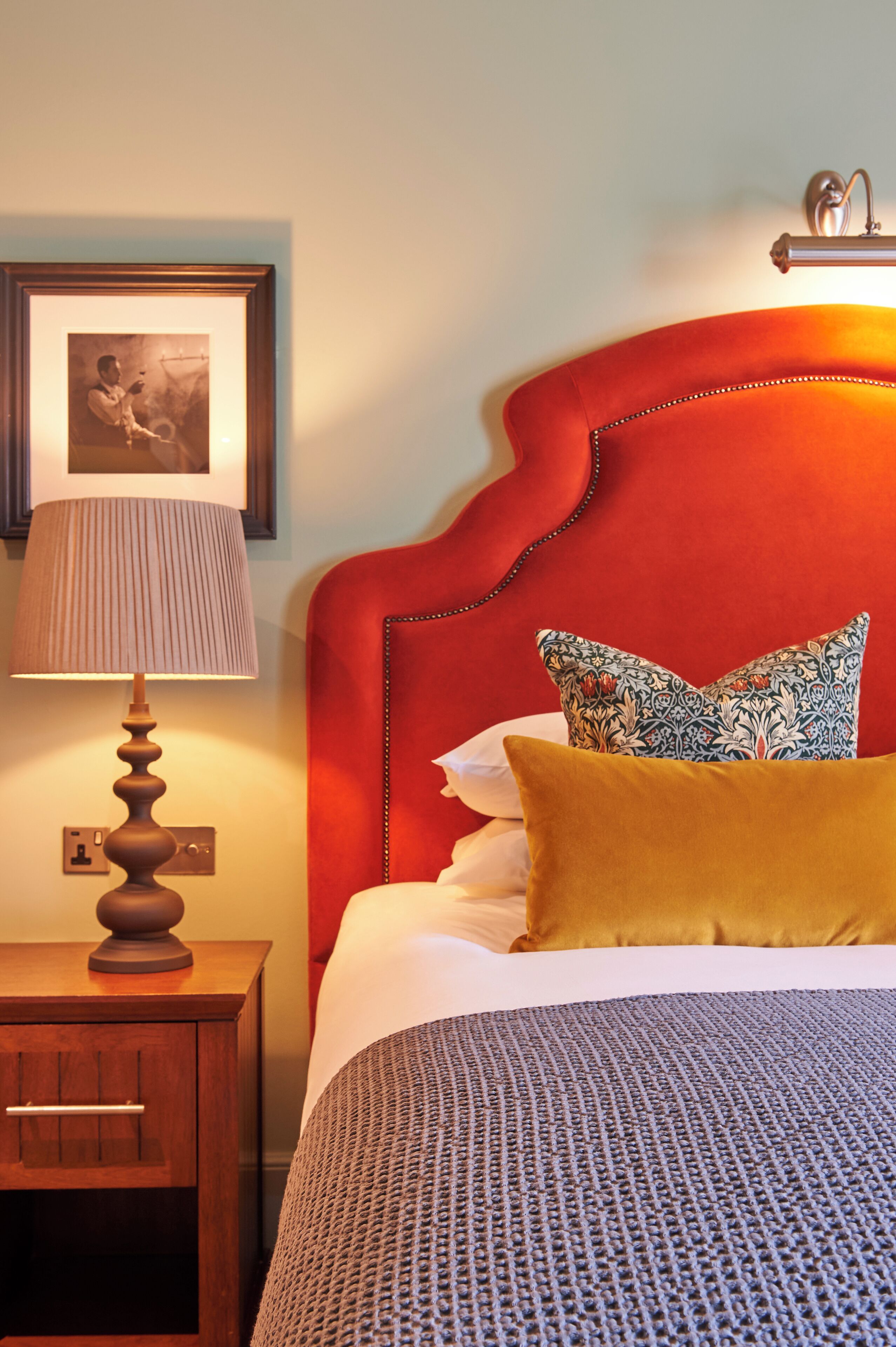 Cama bem arrumada com colcha estampada, cabeceira vermelha e duas almofadas decorativas.
