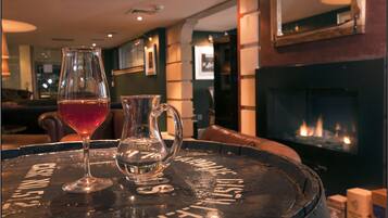 Un coin bar avec une cheminée, une table ronde avec un pichet en verre et un verre à vin, et des sièges en cuir.