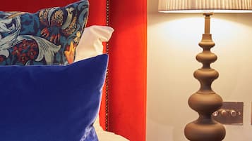 Een bed met een rode hoofdbord, blauw-witte kussens, en een houten nachtkastje met een lamp.