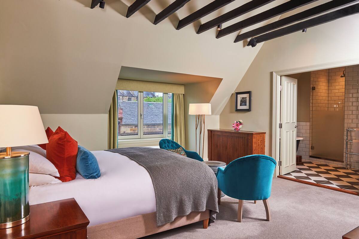 A bedroom with a bed, a nightstand, a lamp, a chair, a dresser, and a bathroom visible through an open door.