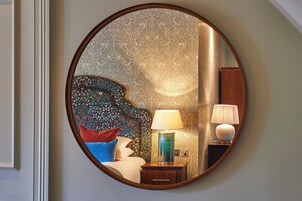 A round mirror reflecting a bed with a floral headboard, two bedside lamps, and a nightstand.