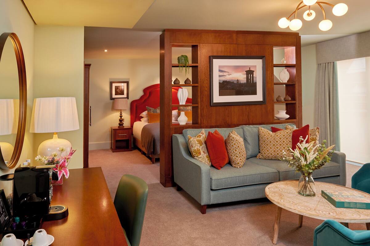 A hotel room with a sofa, a coffee table, a dining table, and a bookshelf.