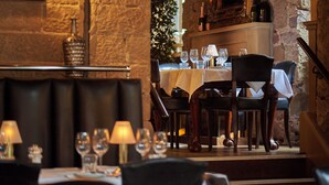Un restaurant amb parets de pedra, seients de cuir i una taula preparada amb copes de vi i una espelma.