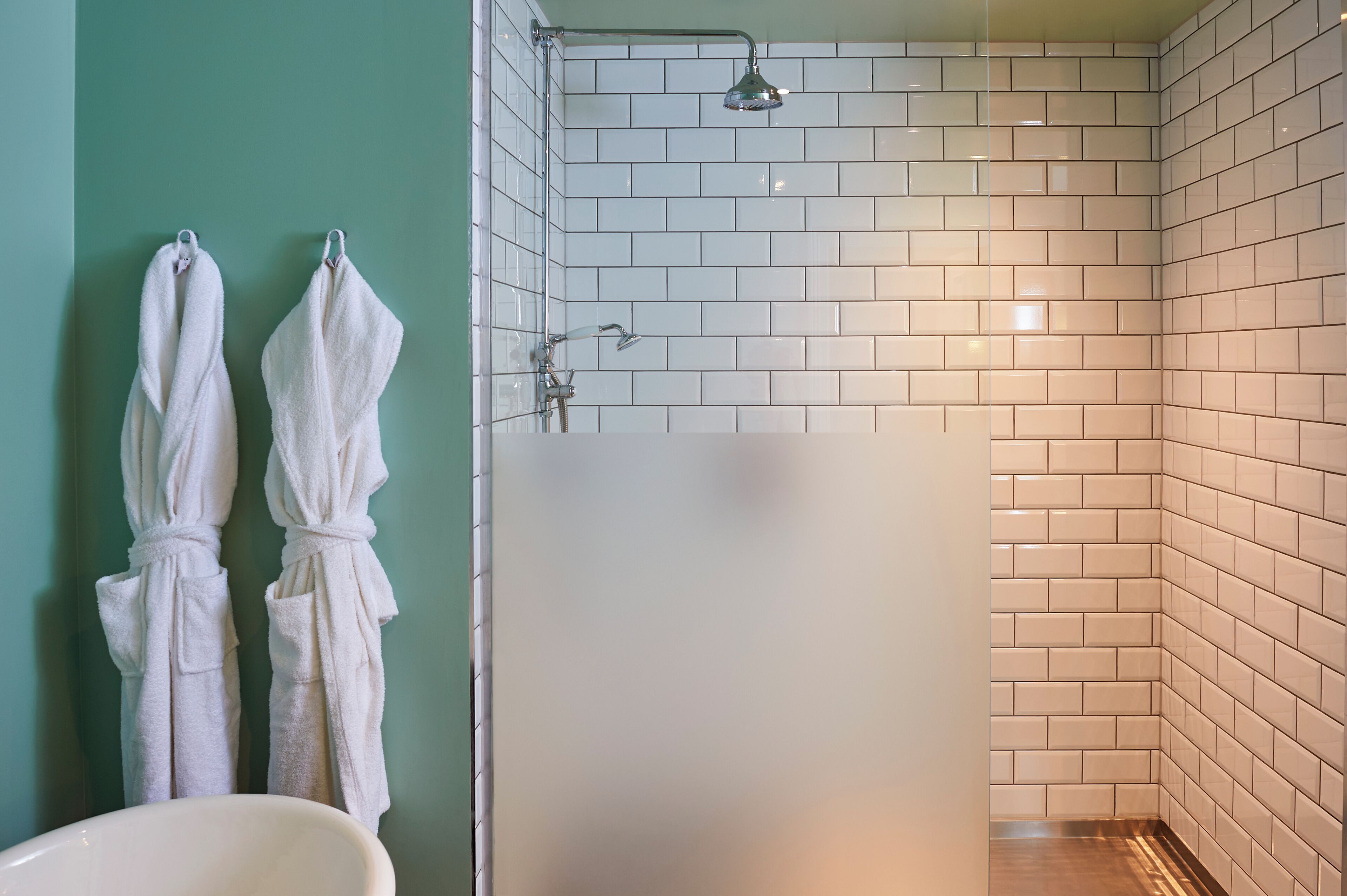 A bathroom with white tiled walls, a shower with a handheld showerhead, and two white towels hanging on a rack.