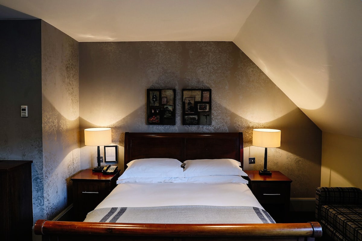 A neatly made bed with white linens, two bedside lamps, and a framed picture above the headboard.