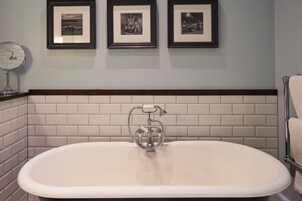 A bathroom with a freestanding bathtub, a mirror, and three framed photographs on the wall.