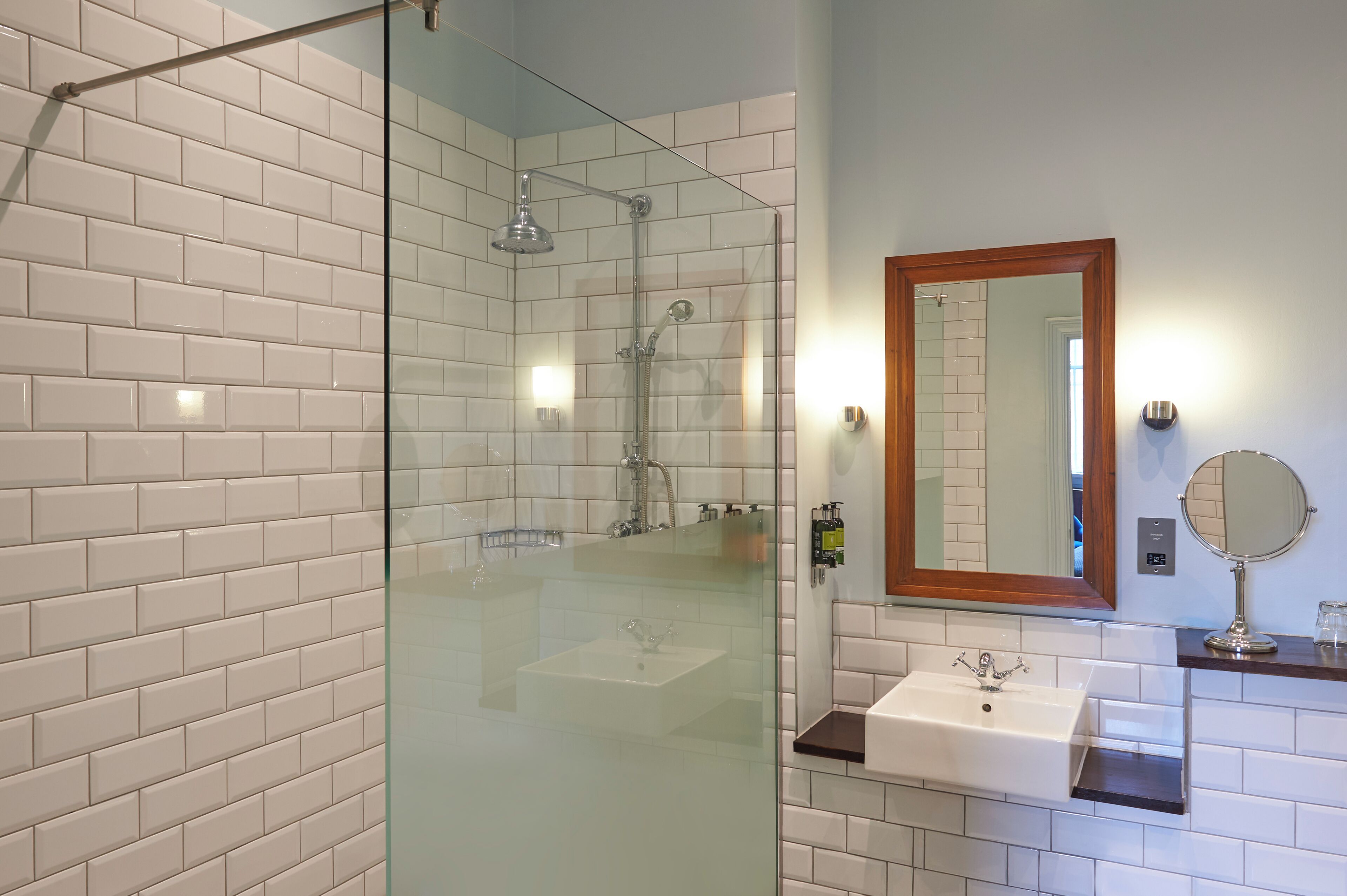A bathroom with a glass-enclosed shower, a white sink, and a mirror with a wooden frame.