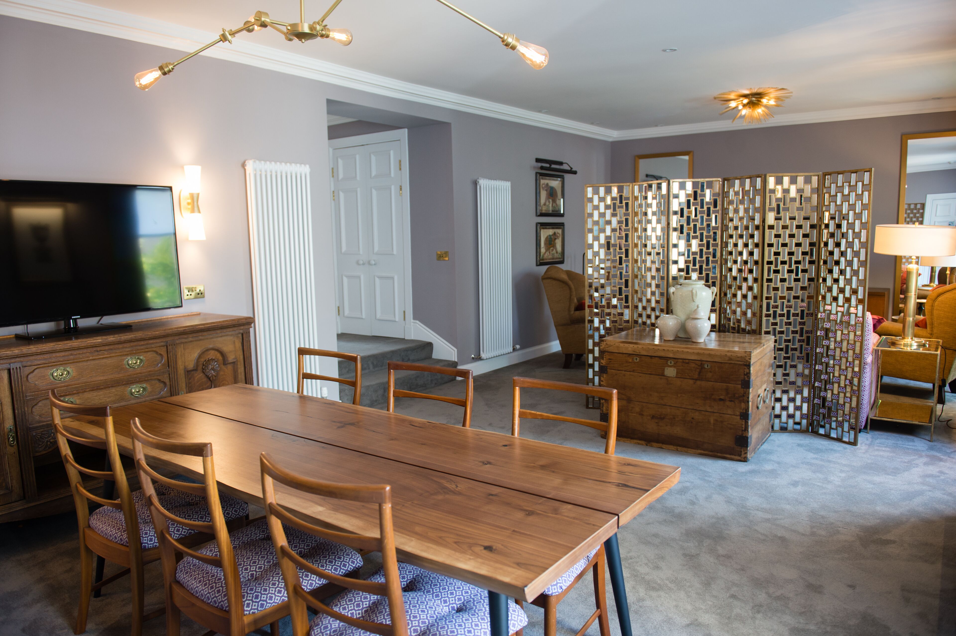 Un comedor con una mesa y sillas de madera, televisor y un separador decorativo.