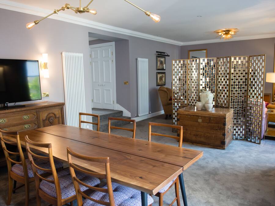 Un comedor con una mesa y sillas de madera, televisor y un separador decorativo.