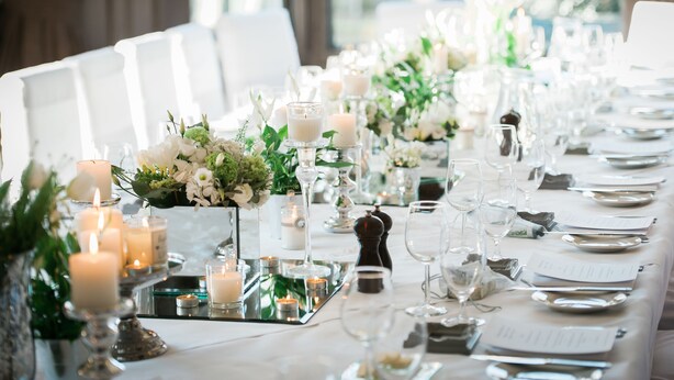 Uma longa mesa de jantar posta com velas, flores e taças, sugerindo um evento gastronômico formal.