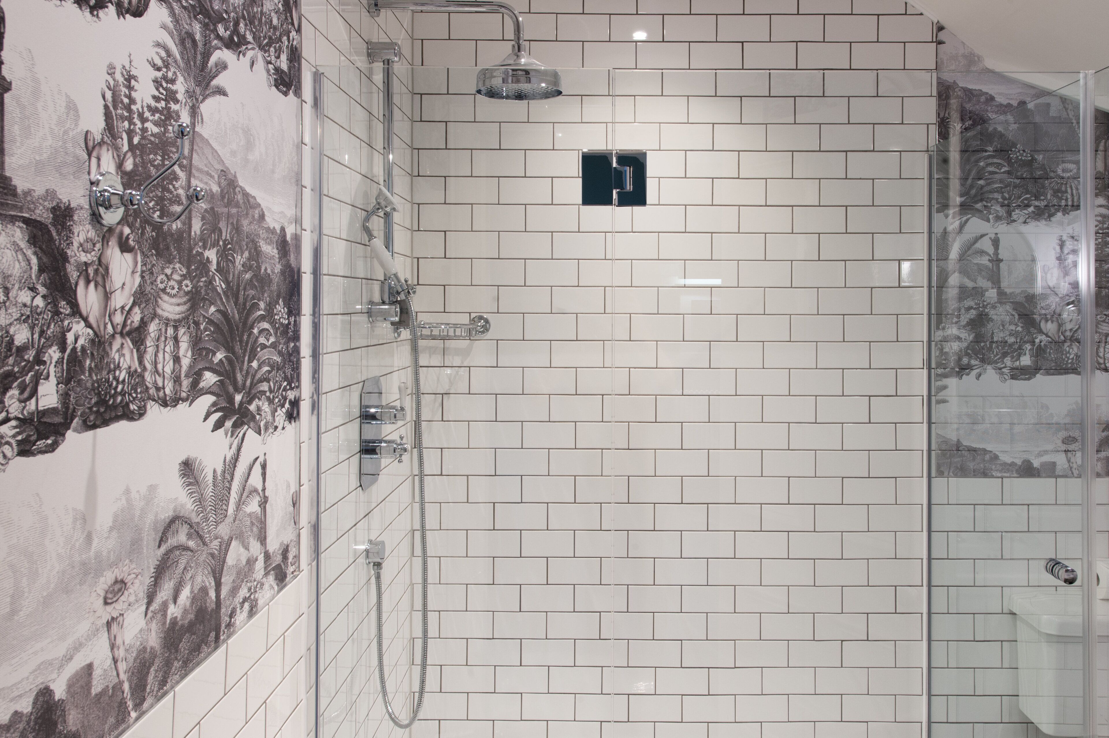 A bathroom with white tiled walls, a shower with a glass door, and a mural of a tropical scene.