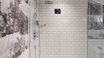 A bathroom with white tiled walls, a shower with a glass door, and a mural of a tropical scene.